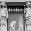 Dos estatuas de Atlantes mirando hacia una ventana en la que se ve a dos mujeres de espaldas en ropa interior