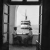 Un paer de hombre charlando con un barco que se aleja (fotografía: Santorini 1954 @Robert MacCabe)