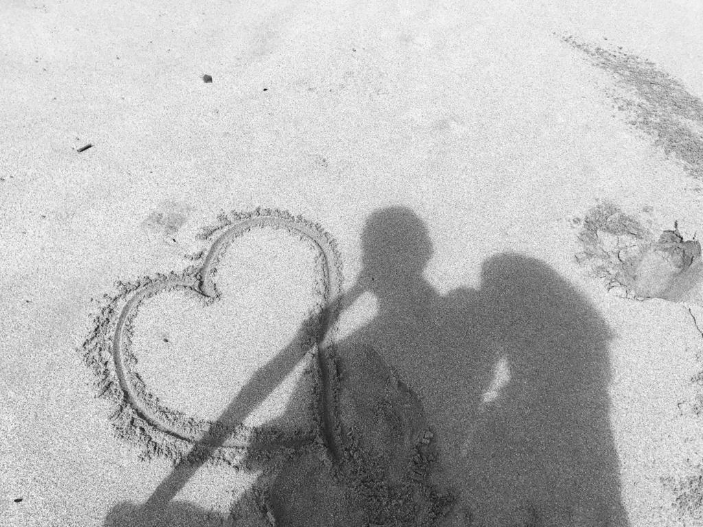 La sombre de una pareja sobre un corazon dibujado en la arena
