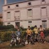 Grupo de niños con bicicletas en un jardí delante de una casa de ladrillo de varias plantas (Foto cedida por Sonsoles Maroto a Tierra Trivium)