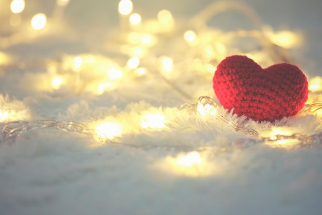 un corazón rojo de punto sobre la nieve y unas luces de navidad de color blanco