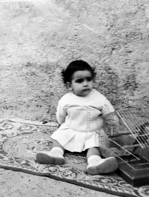 niña morena sentada en una alfombra en mitad de un solar (fotografía familiar de Henar Tejero)
