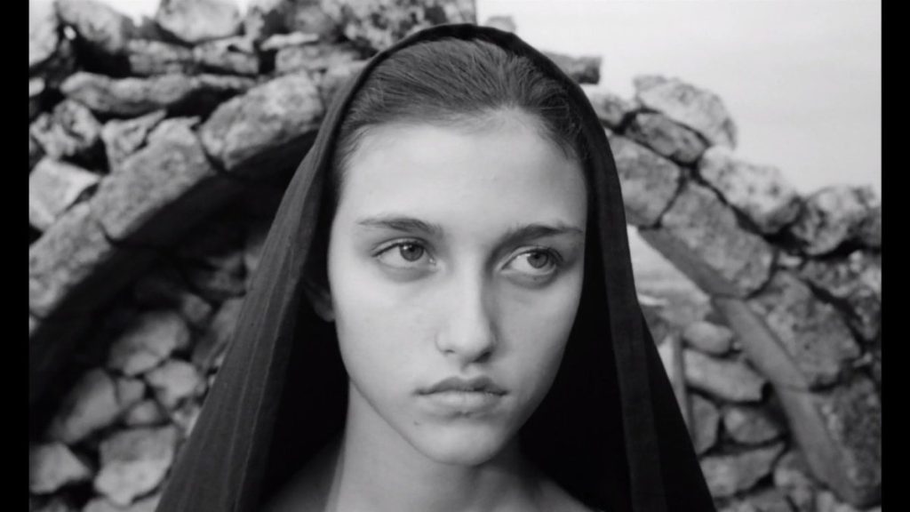 Fotograma de "El Evangelio según San Mateo" ("Il vangelo secondo Matteo", Pier Paolo Pasolini, 1964), en el que se ve el rostro de una chica con una toca negra delante de los restos de un arco de piedra.